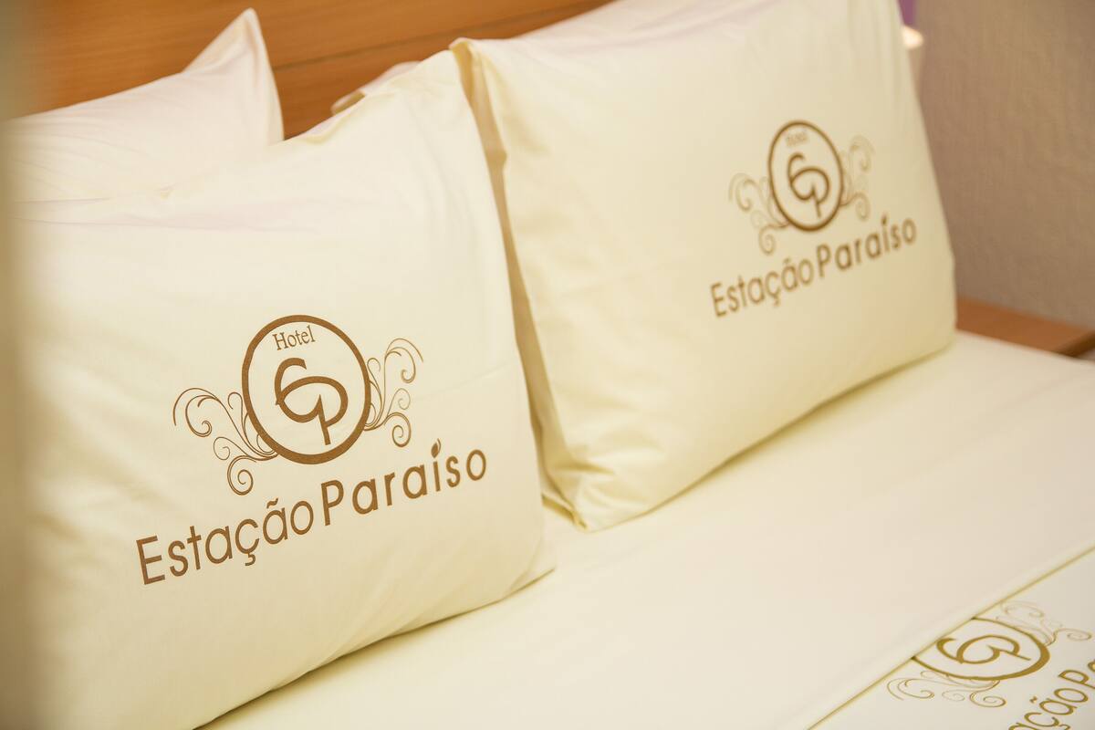 Two pillows with the logo "Estação Paraíso" on a bed.