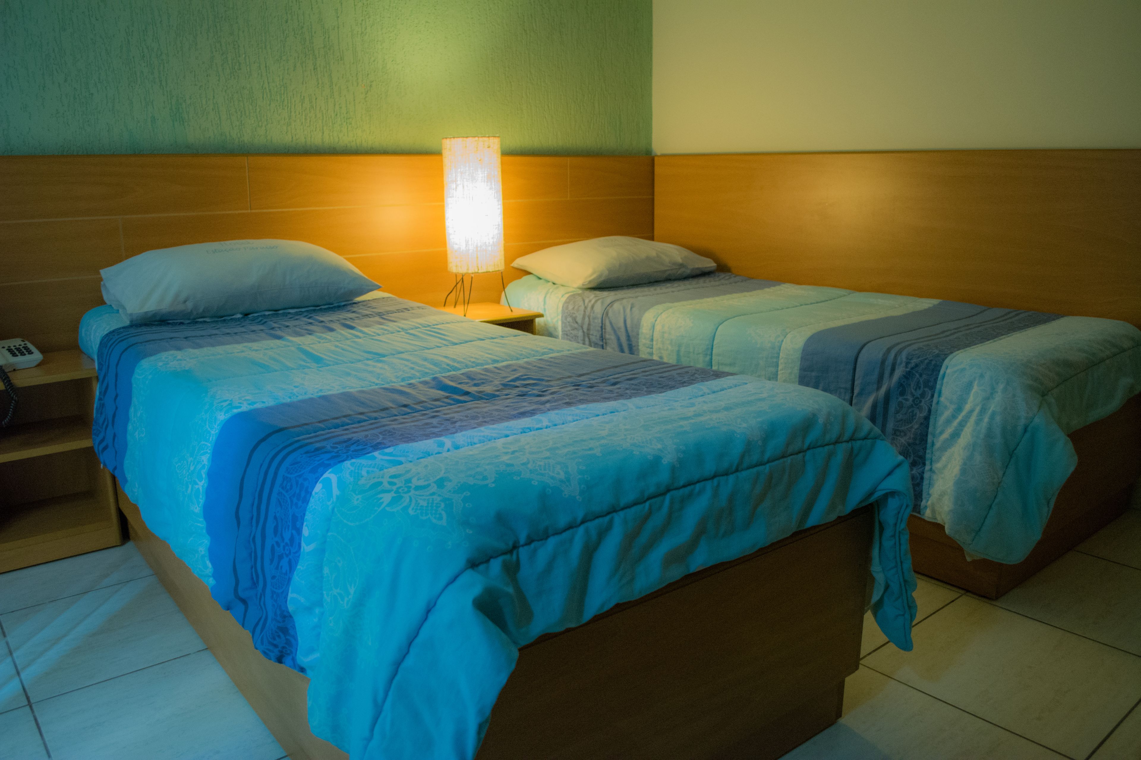 A hotel room with two single beds, a nightstand with a lamp, and a wooden headboard.