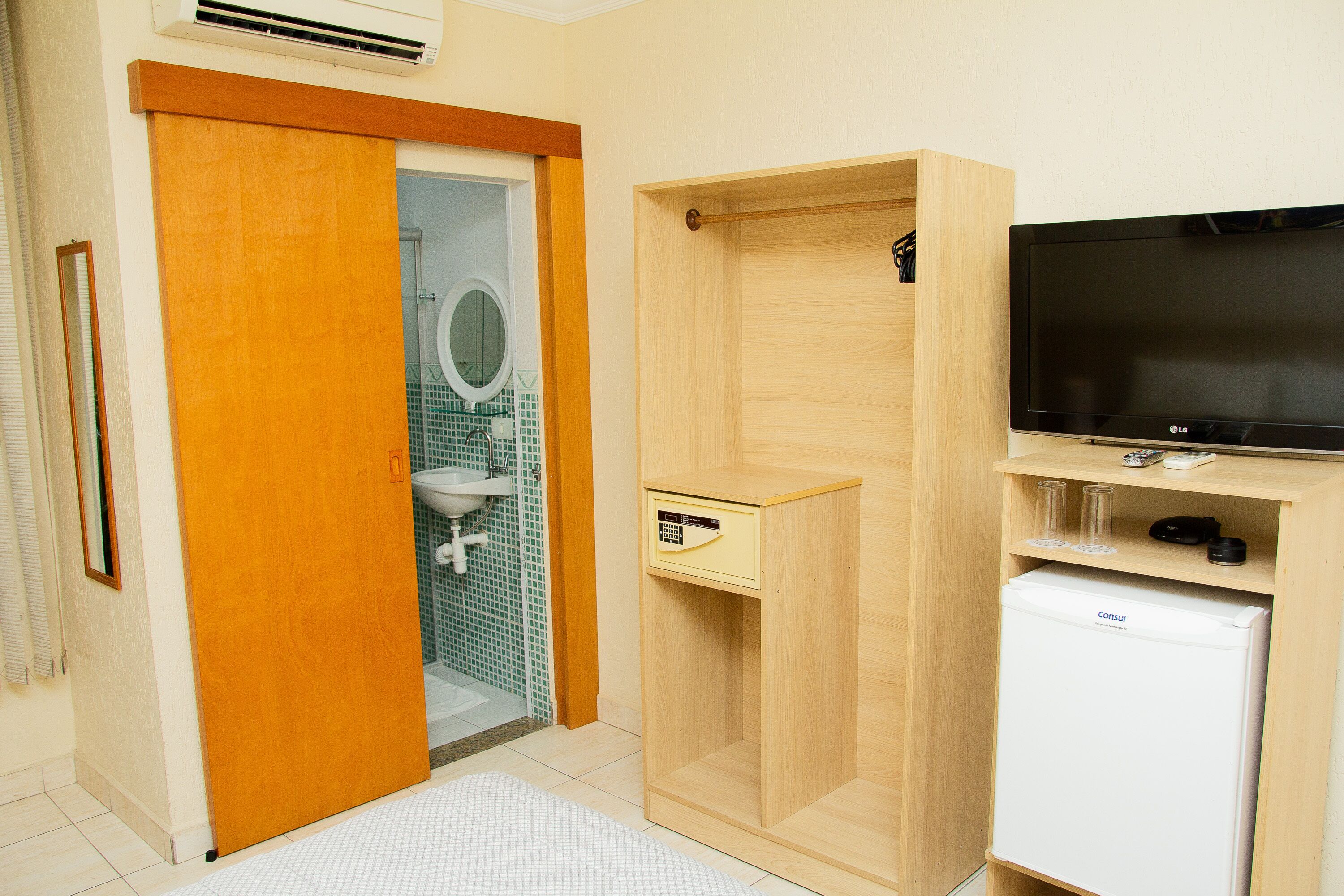 Een kleine badkamer met toilet, wastafel, spiegel en een televisie op een houten kast.