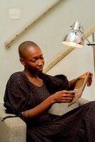 Una persona seduta su un divano che legge un libro sotto una lampada da tavolo.
