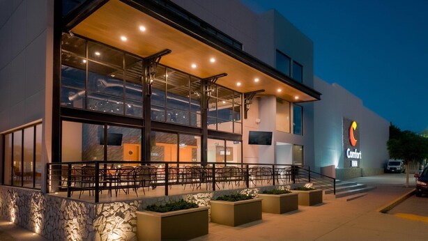 Un hôtel Comfort Inn doté d’un espace extérieur abrité avec des sièges, de grandes fenêtres et une façade en pierre.