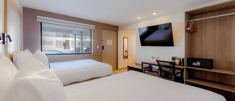 Ein Hotelzimmer mit einem großen Bett, einem Schreibtisch mit Stuhl, einem an der Wand befestigten Fernseher und einem Fenster mit Blick nach draußen.