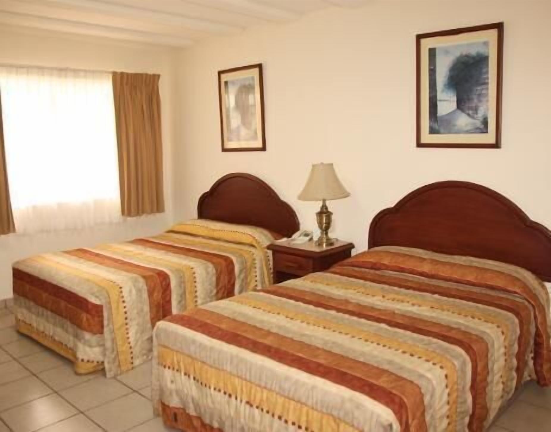 A hotel room with two beds, a nightstand with a lamp, and two framed pictures on the wall.