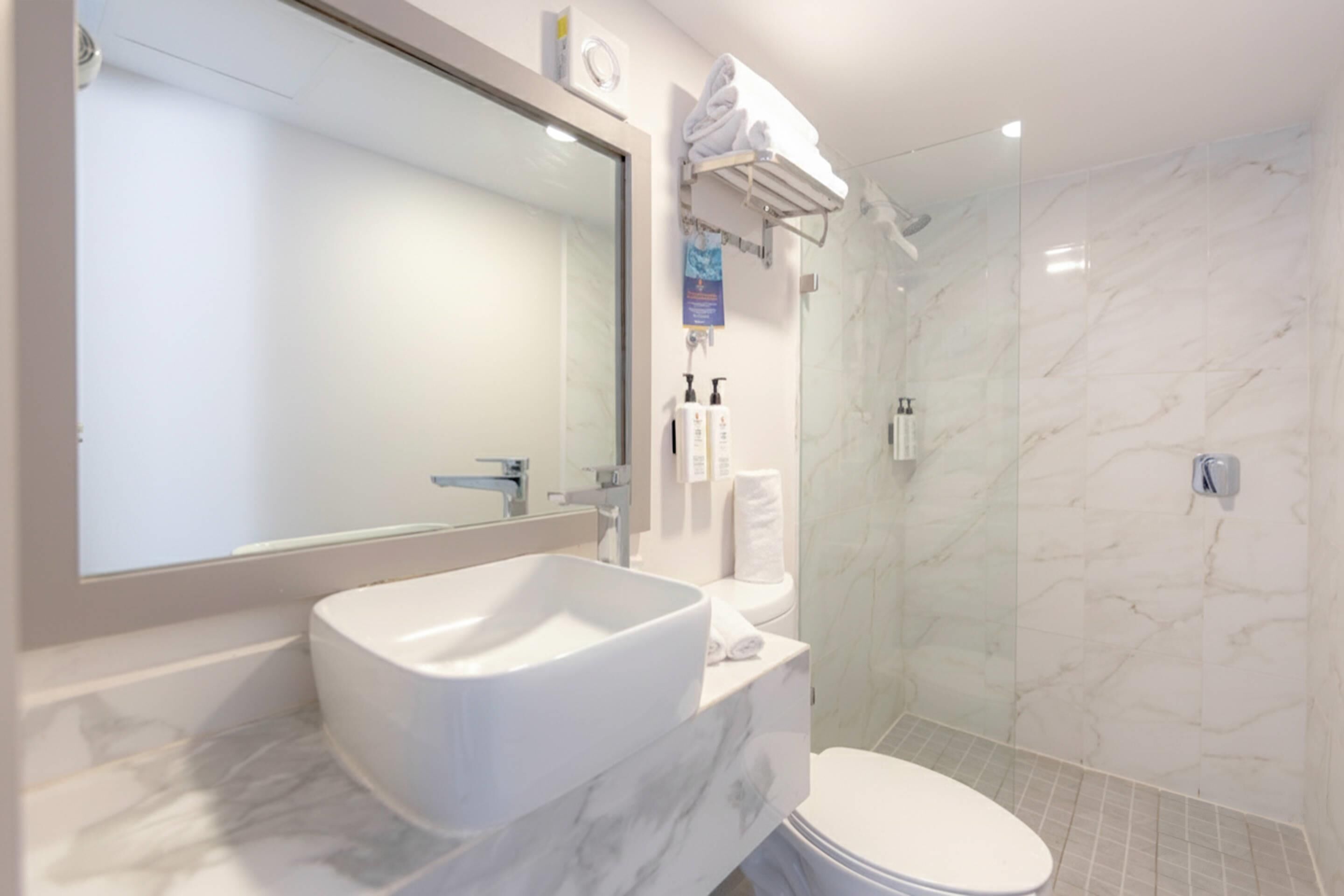 A bathroom with a large mirror, a white sink, a toilet, and a shower area.