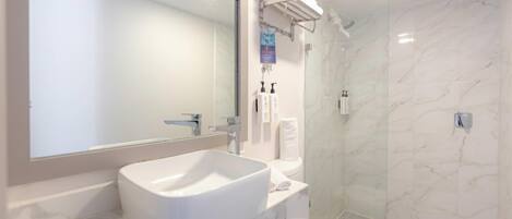 A bathroom with a large mirror, a white sink, a toilet, and a shower area.