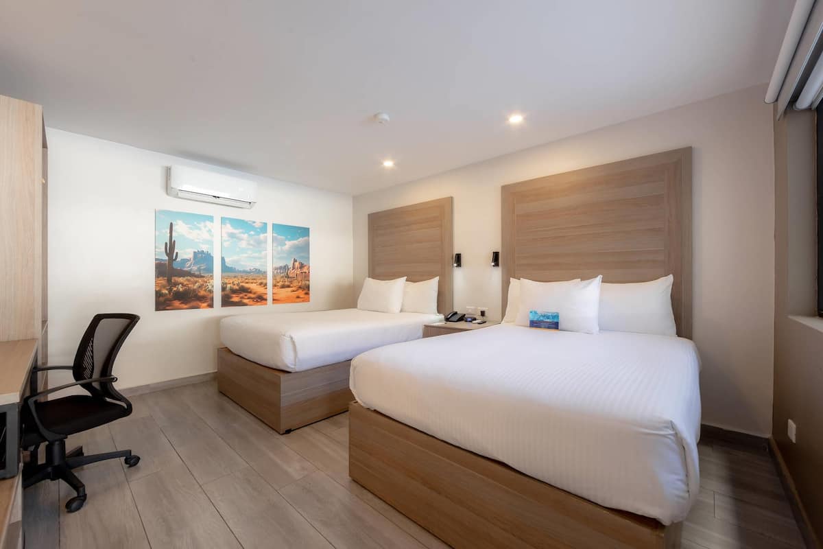 Habitación de hotel con dos camas individuales, un escritorio con silla y aire acondicionado de pared.