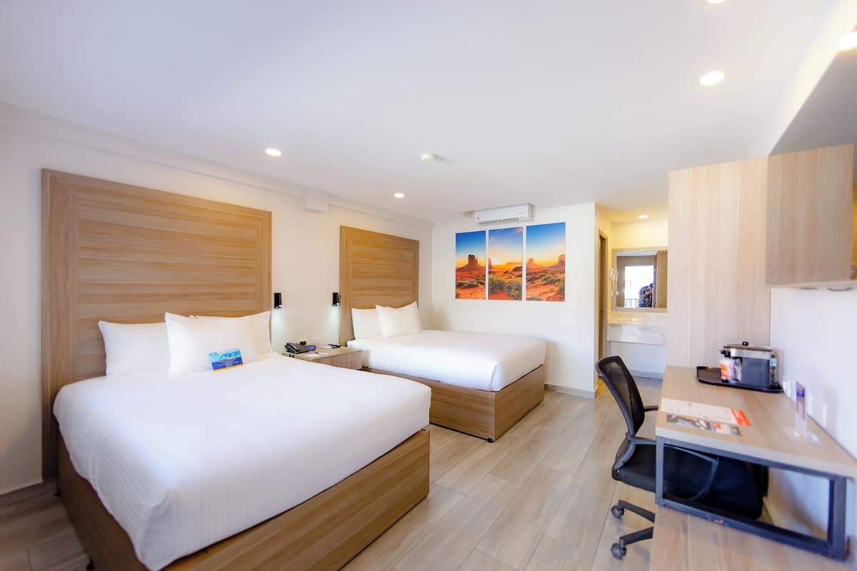 Habitación de hotel con dos camas, un escritorio, una silla y aire acondicionado instalado en la pared.
