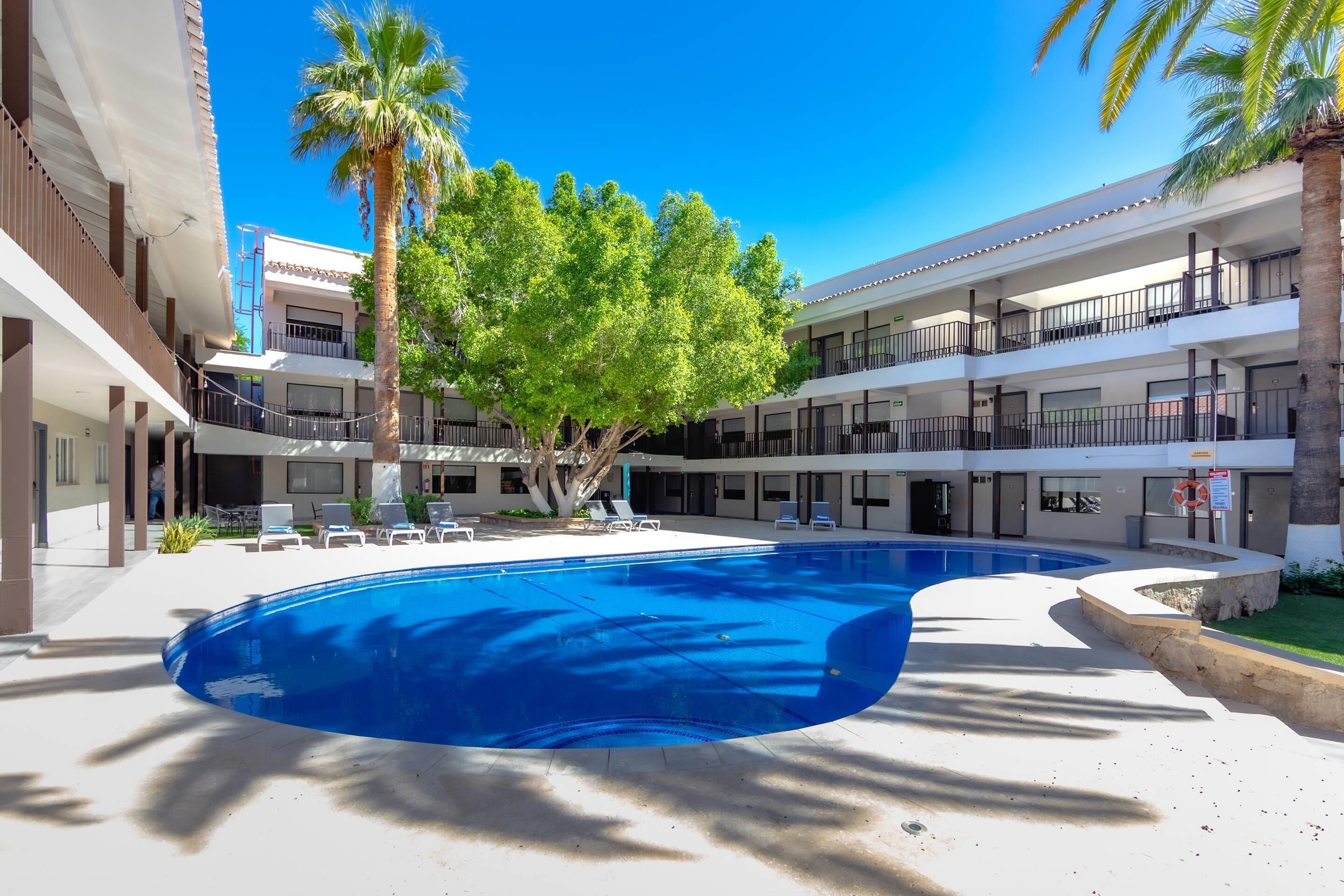 A swimming pool surrounded by palm trees and a multi-story building with balconies.