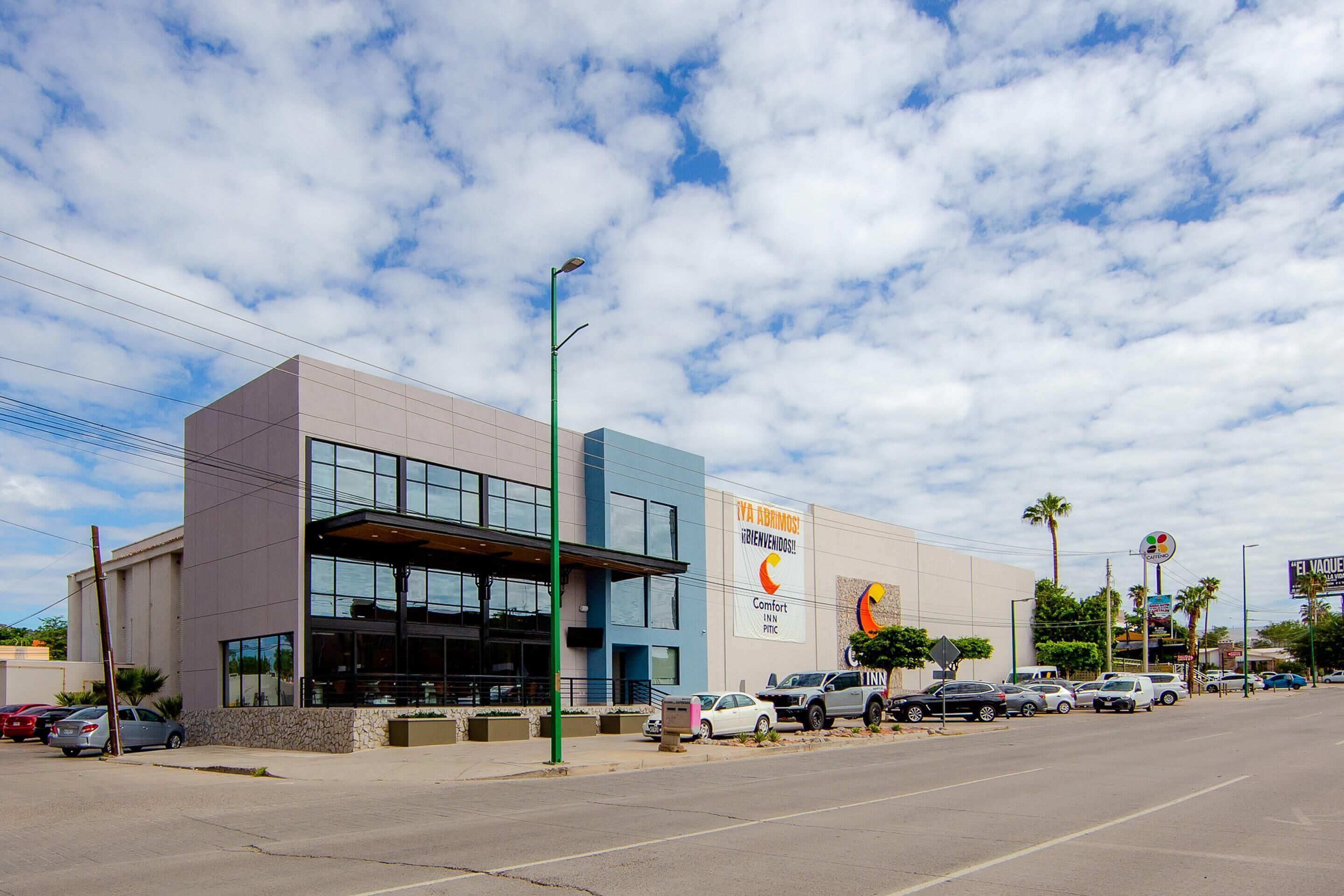 A modern building with a large glass entrance, a Comfort Inn sign, and a parking lot with several cars.