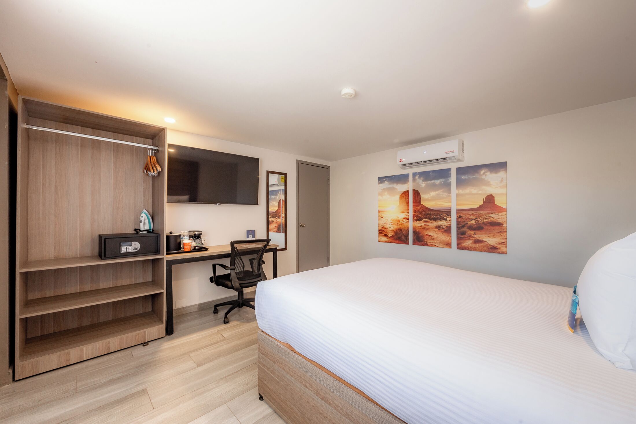 A hotel room with a bed, a desk with a chair, a wardrobe, and a mounted TV.