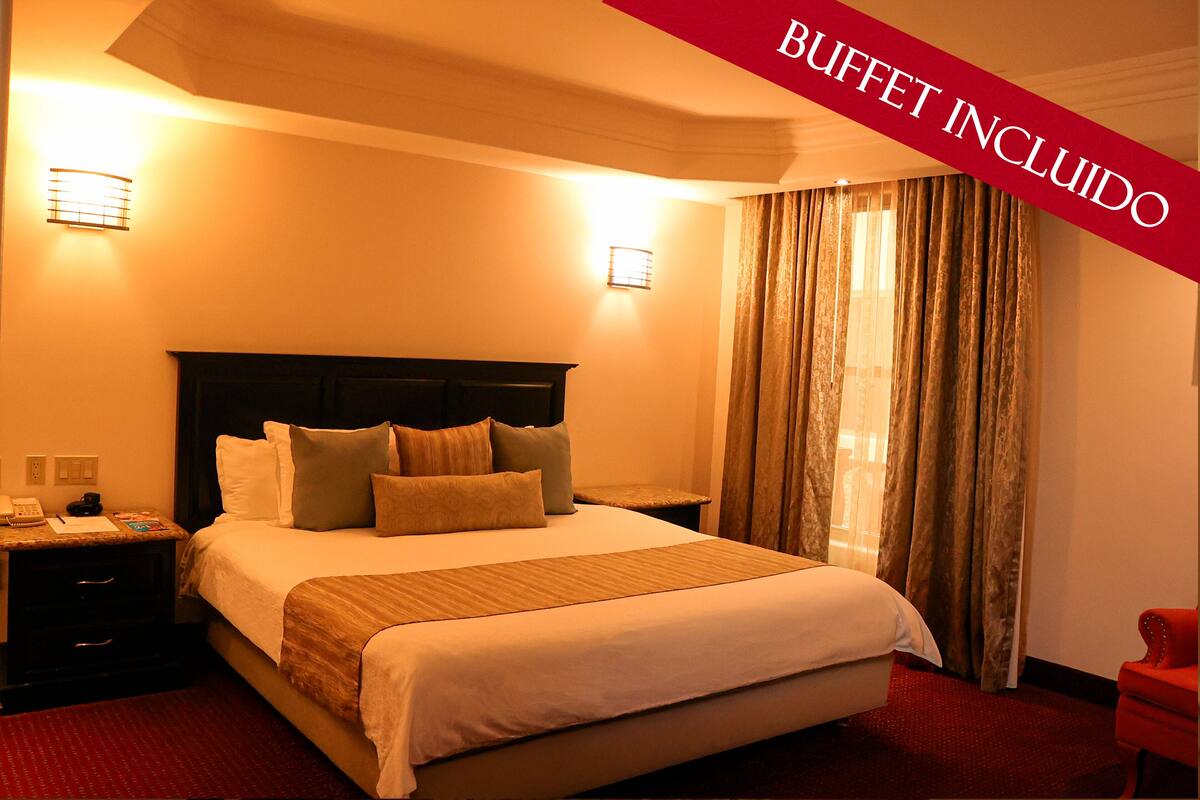 Une chambre d’hôtel avec un lit, des tables de chevet et un fauteuil rouge.