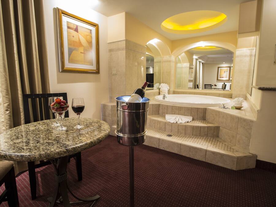 Un baño de hotel con un lavamanos de mármol, una bañera y una mesita de mármol con copas de vino.