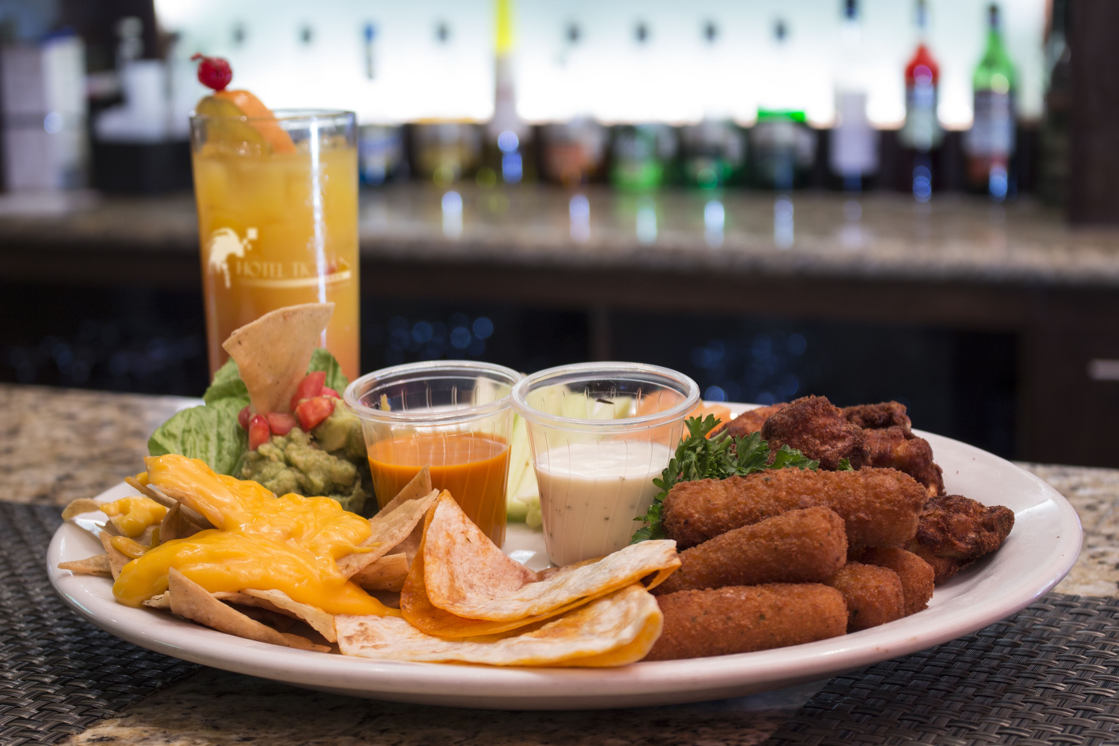 A plate of nachos, guacamole, and a drink with a garnish on a restaurant table.