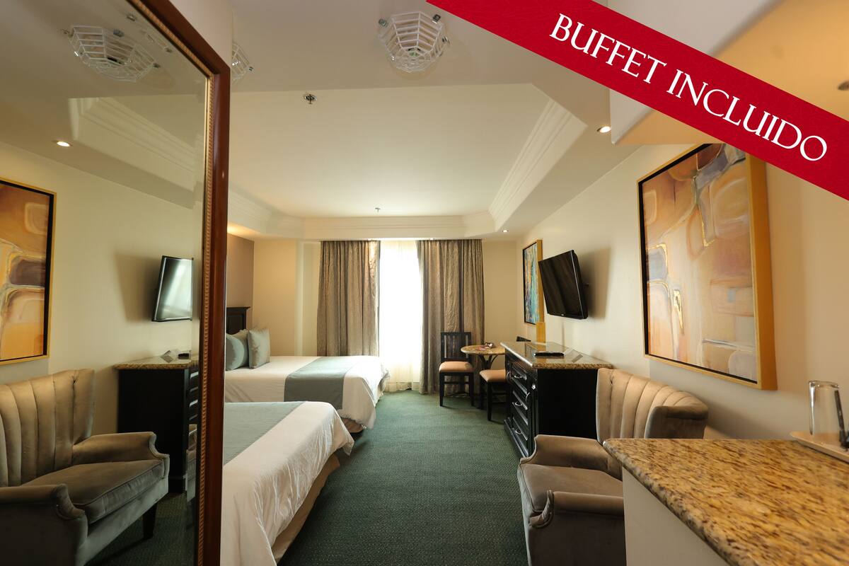 Une chambre d’hôtel avec deux lits, un bureau, une chaise, une télévision et des œuvres d’art accrochées aux murs.