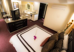 A hotel room with a bed, a TV, a desk with a computer, a bathroom with a sink and mirror, and a window with curtains.