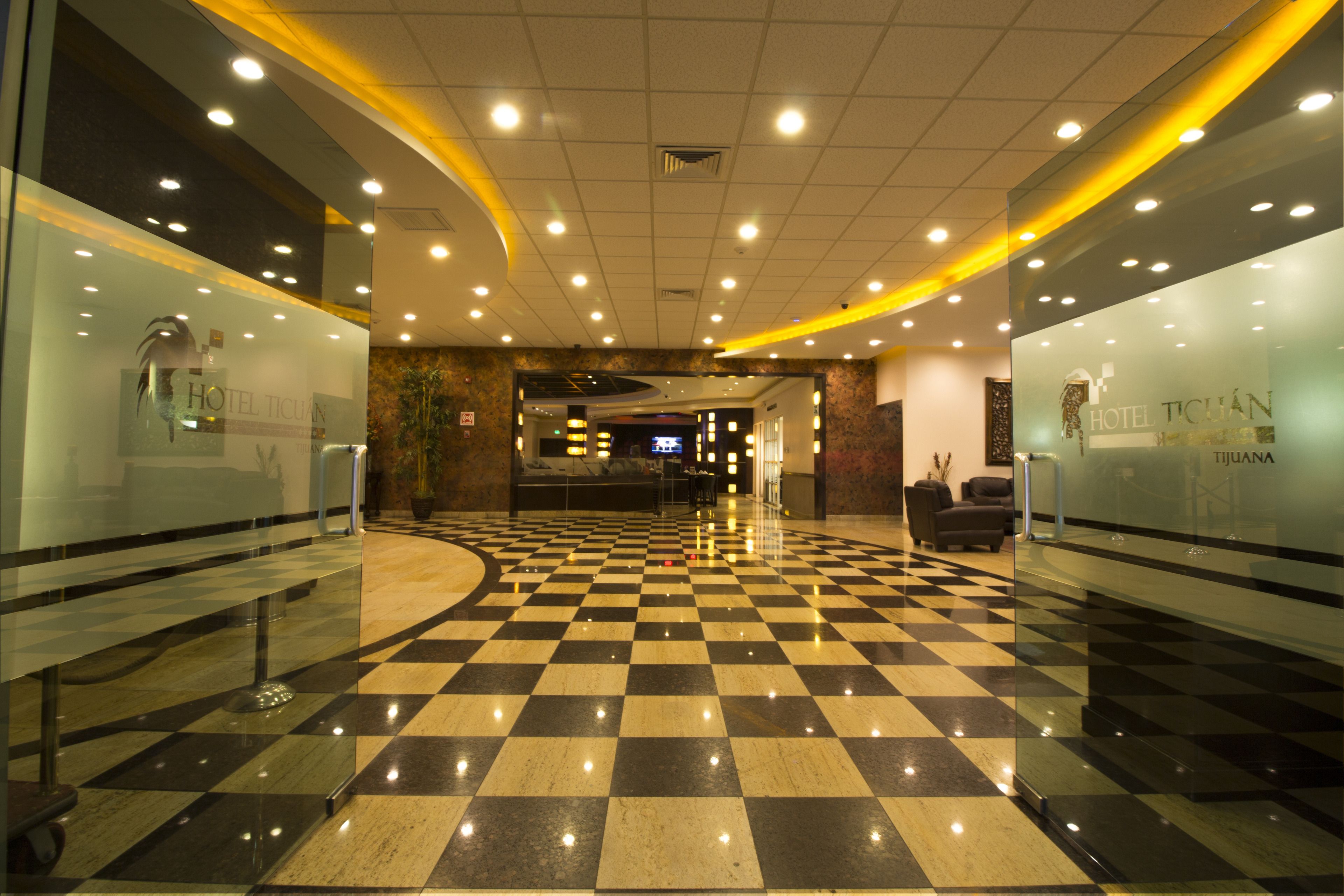 A hotel lobby with a checkered floor, glass walls, and a reception desk.