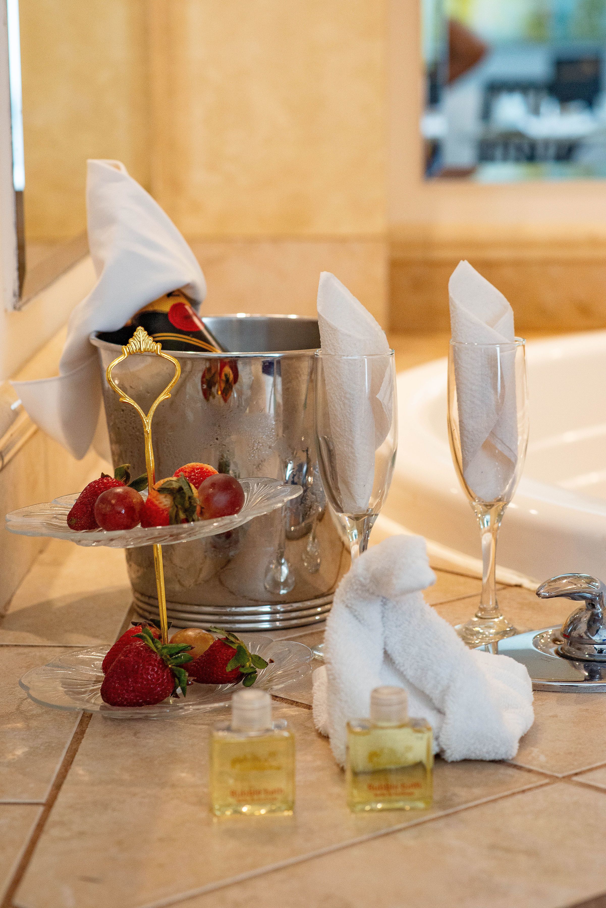 Un baño lujoso con cubo de champán, dos copas de champán, fresas, una botella de perfume y una toalla suave.