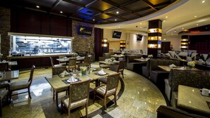 A hotel restaurant with a central bar, dining tables, and booths. - Hotel Ticuán (Tijuana)