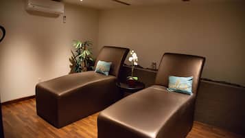 A room with two brown leather chairs, each with a pillow, a small table with a plant, and an air conditioning unit on the wall.