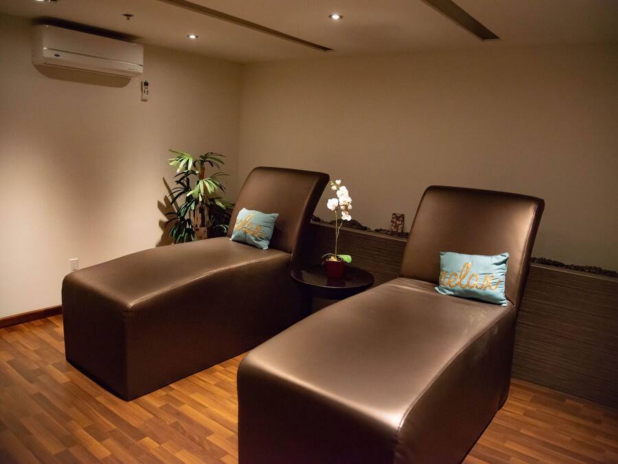 A room with two brown leather chairs, each with a pillow, a small table with a plant, and an air conditioning unit on the wall.