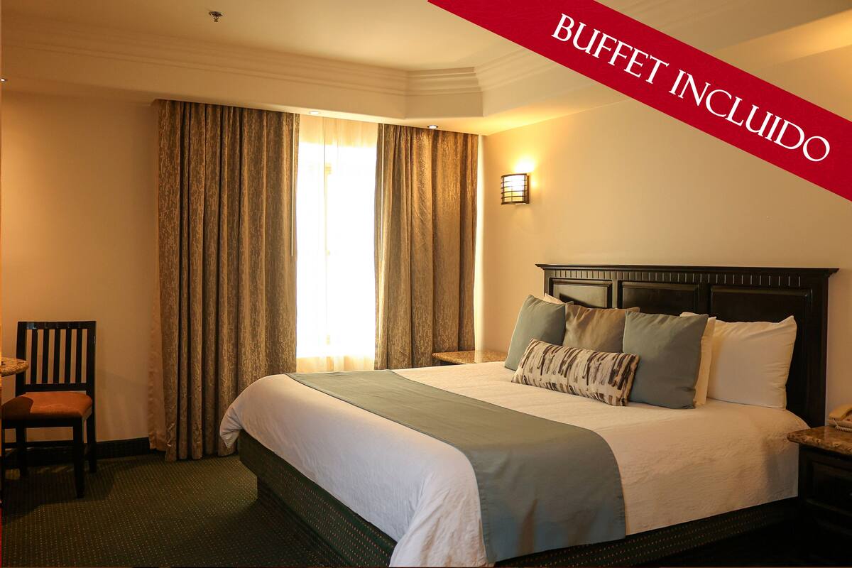 Une chambre d’hôtel avec un grand lit, une chaise, une table de chevet et une lampe fixée au mur.
