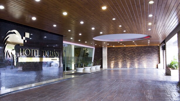 A hotel lobby with a modern design, featuring a wooden ceiling, a large reception desk, and a stone wall. - Hotel Ticuán (Tijuana)