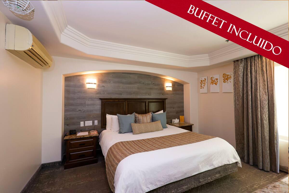Une chambre d’hôtel avec un grand lit, une tête de lit en bois, deux tables de chevet et un climatiseur fixé au mur.