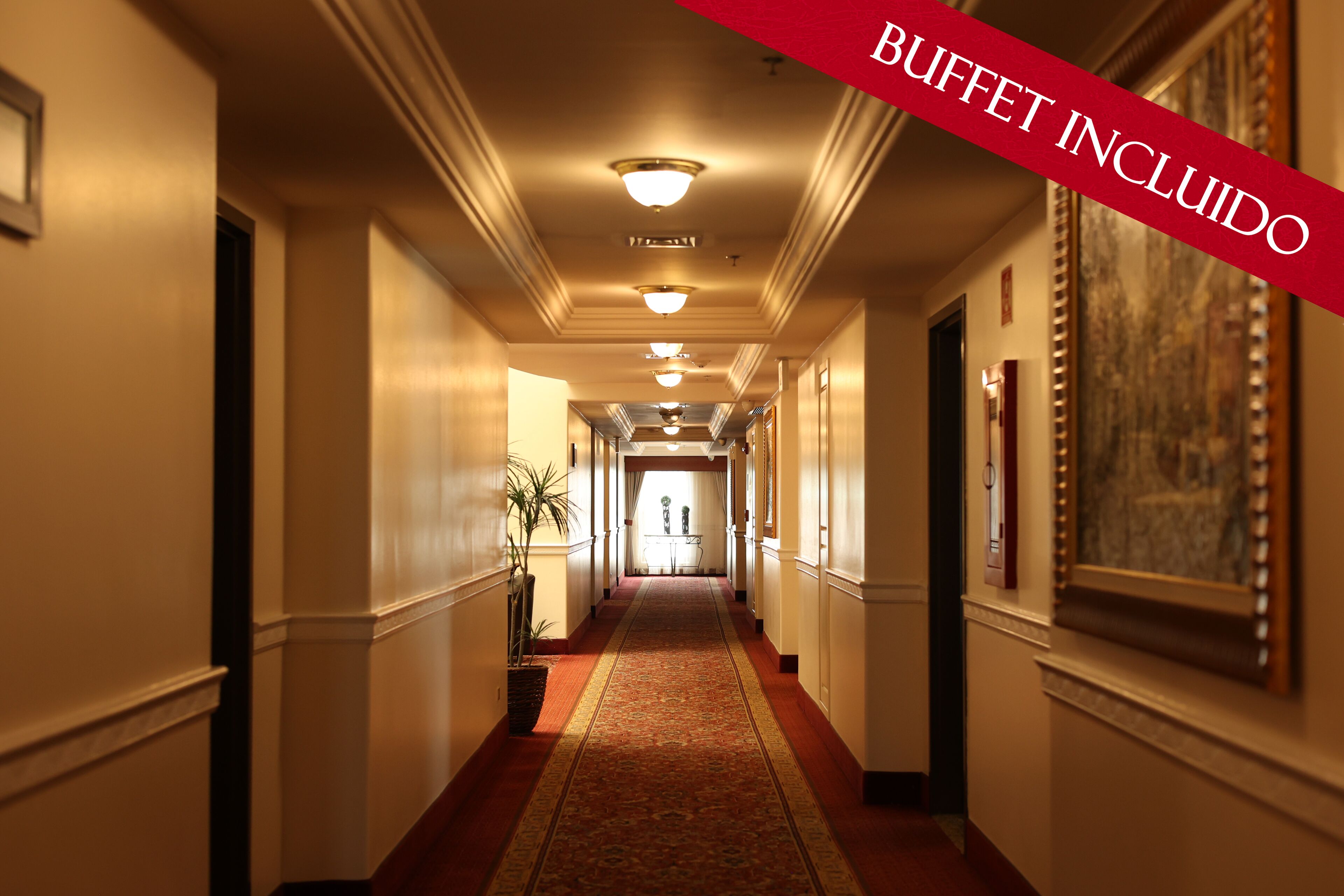 A hotel hallway with a red carpet, framed artwork on the walls, and a buffet area at the end.