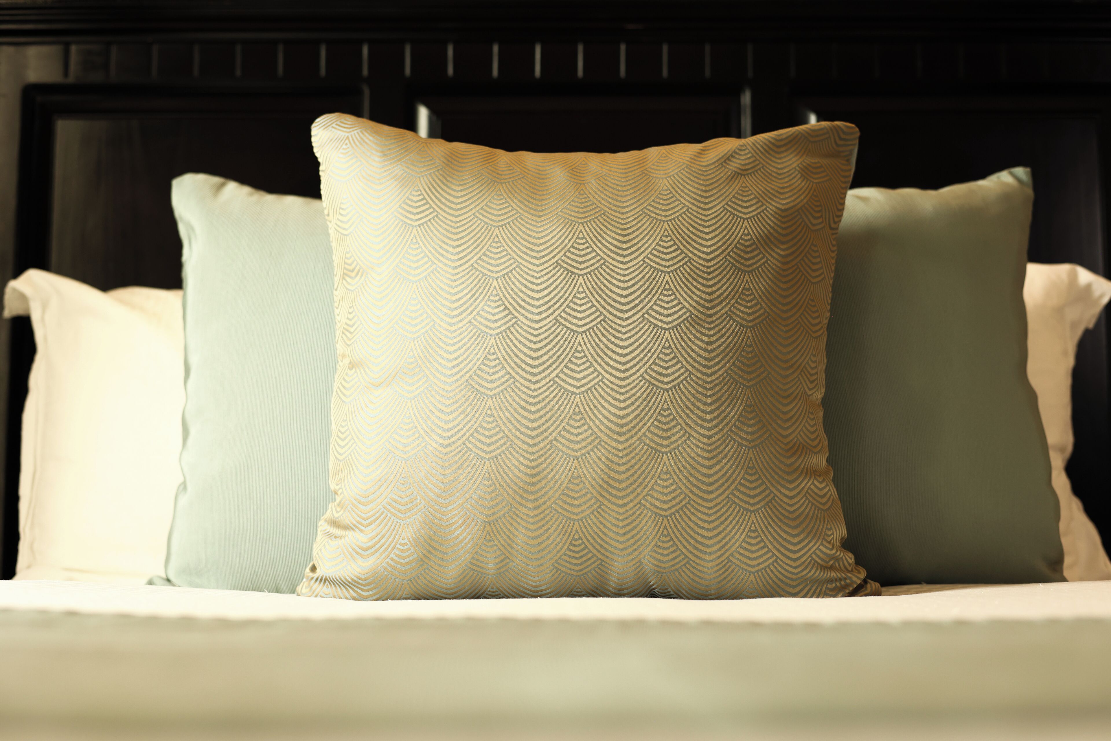 A bed with three pillows, one with a geometric pattern and two plain pillows.