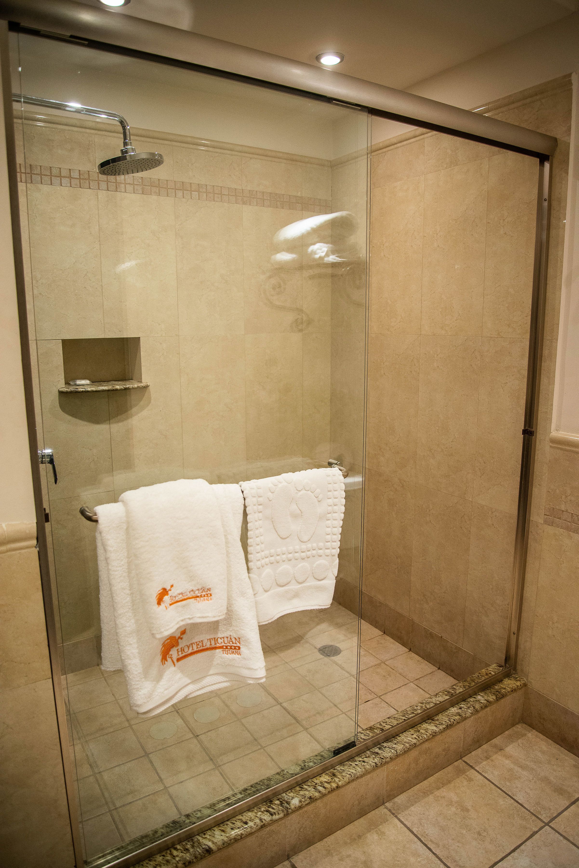 A glass-enclosed shower with a handheld showerhead and a shelf with a soap dish.