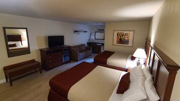 A hotel room with two beds, a TV, a desk, a dresser, a bench, and a painting on the wall.