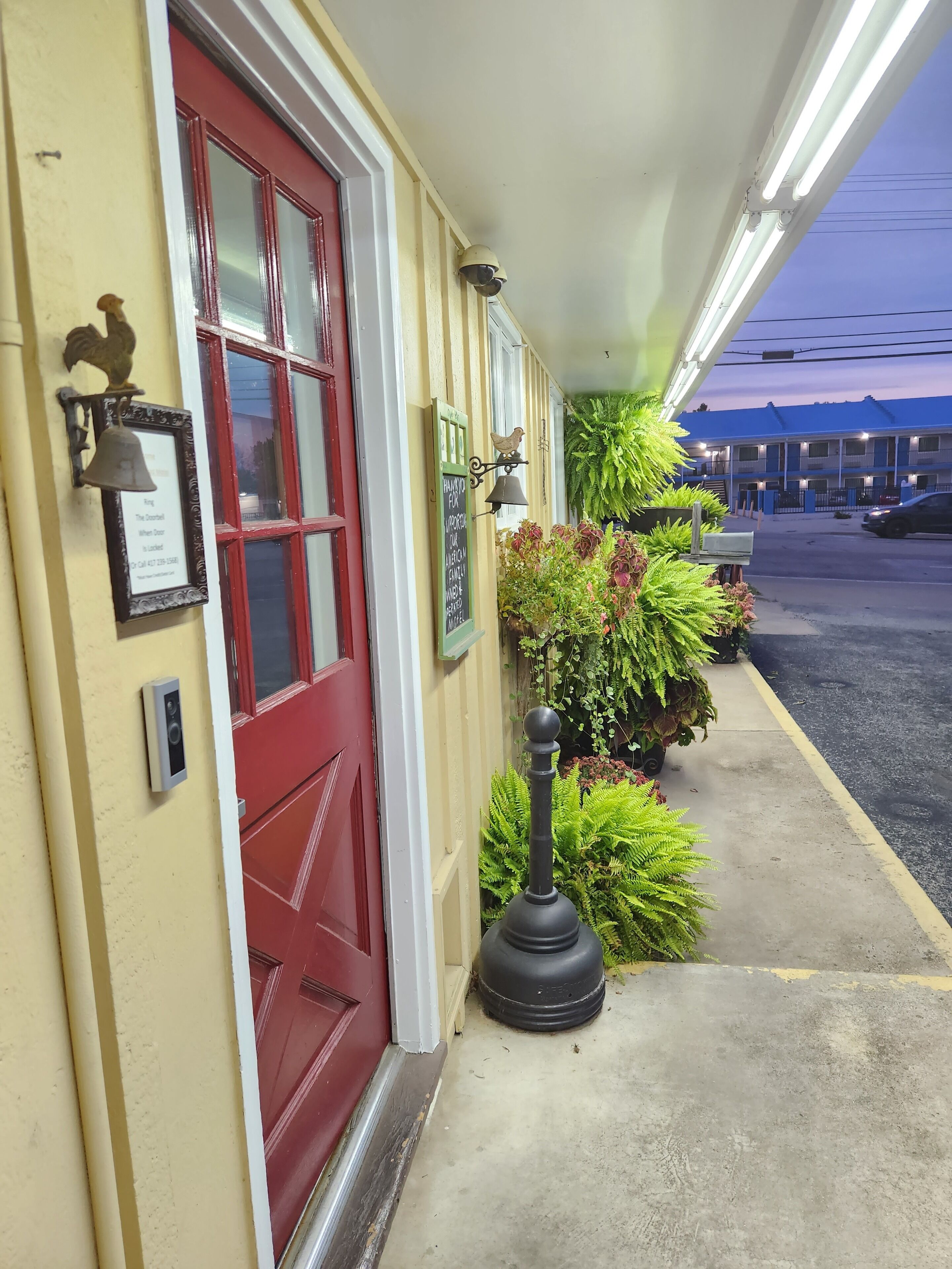 A hotel entrance with a red door, a bell, a security camera, and a signboard.