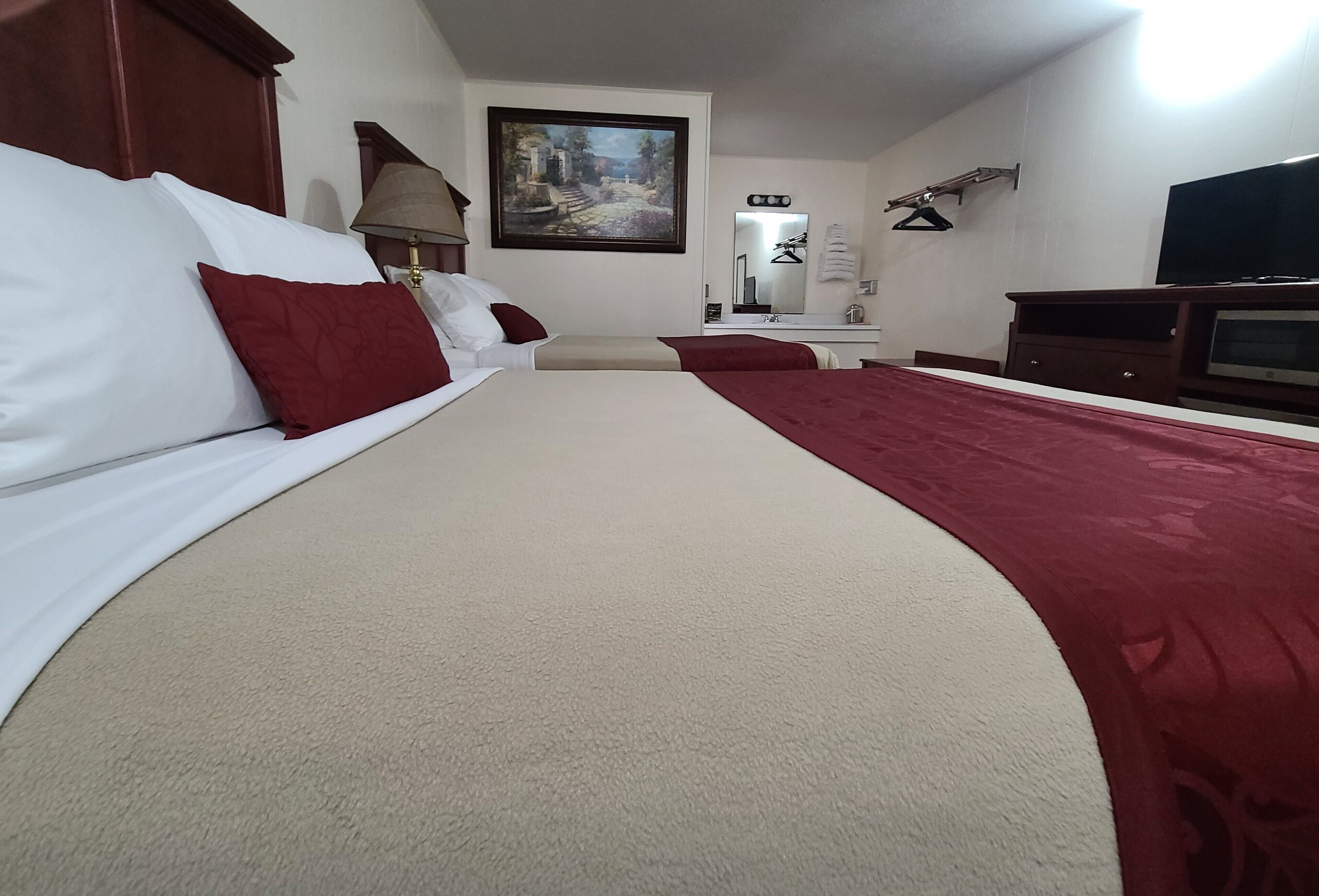 A hotel room with a large bed, a desk with a lamp, a TV, and a painting on the wall.
