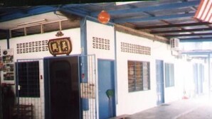 A building with a blue and white exterior, a large door with a metal gate, and a sign with Chinese characters. - ET Budget Guest House (George Town)