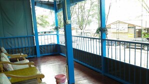 A covered outdoor seating area with wooden chairs and a pink trash bin. - ET Budget Guest House (George Town)