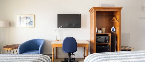 Une chambre d’hôtel avec deux lits, un bureau, une chaise, une télévision, une armoire et une petite table.