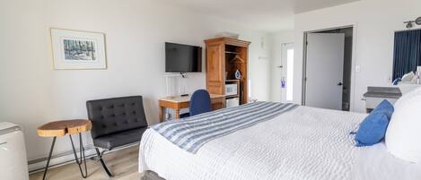 Ein Hotelzimmer mit einem großen Bett, einem Schreibtisch mit Stuhl, einem Fernseher und einem Kleiderschrank.