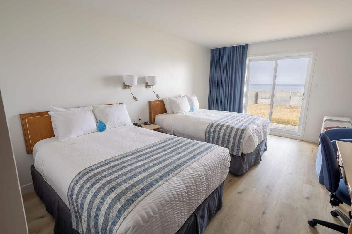 A hotel room with two beds, a desk, and a view of the beach.