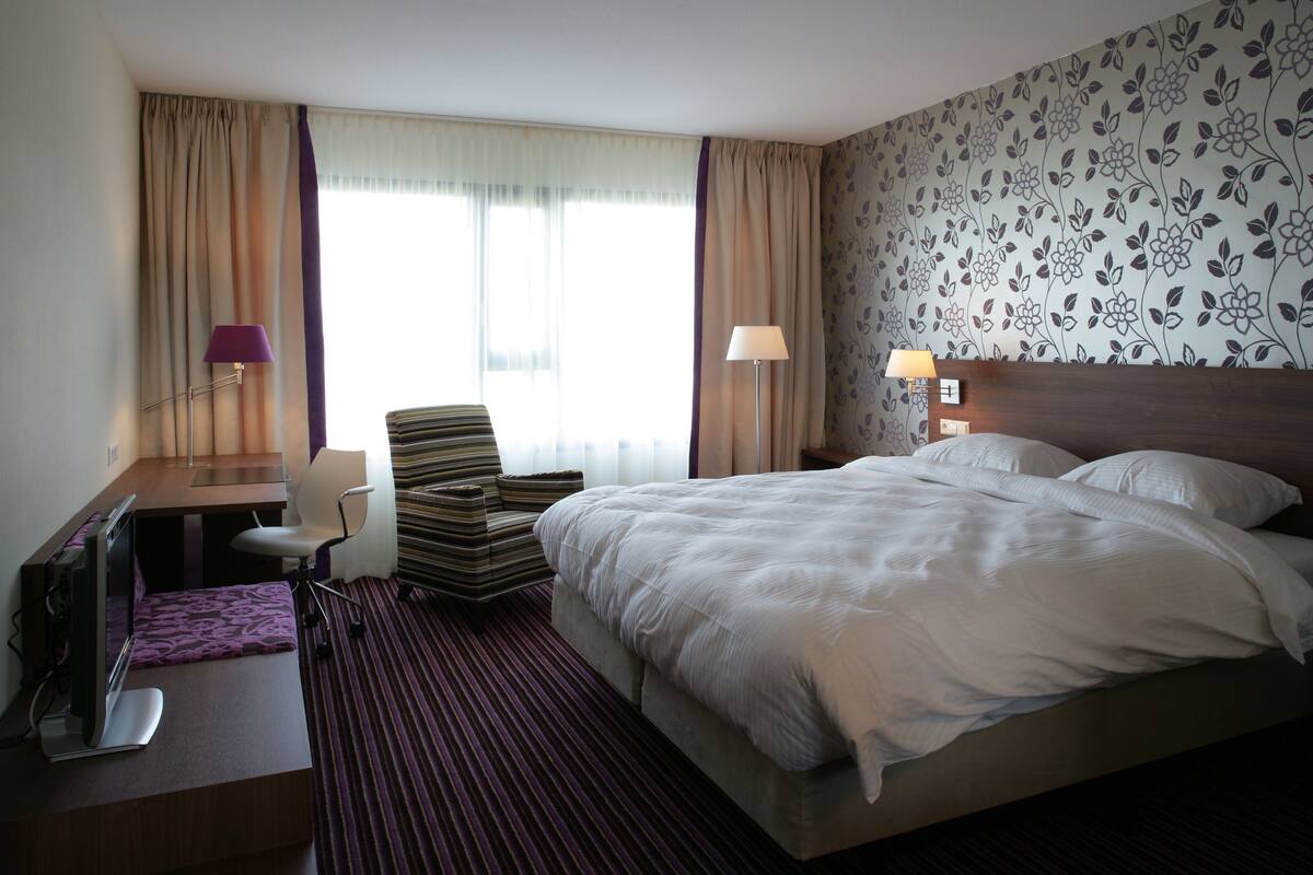 A hotel room with a bed, desk, chair, and lamps.
