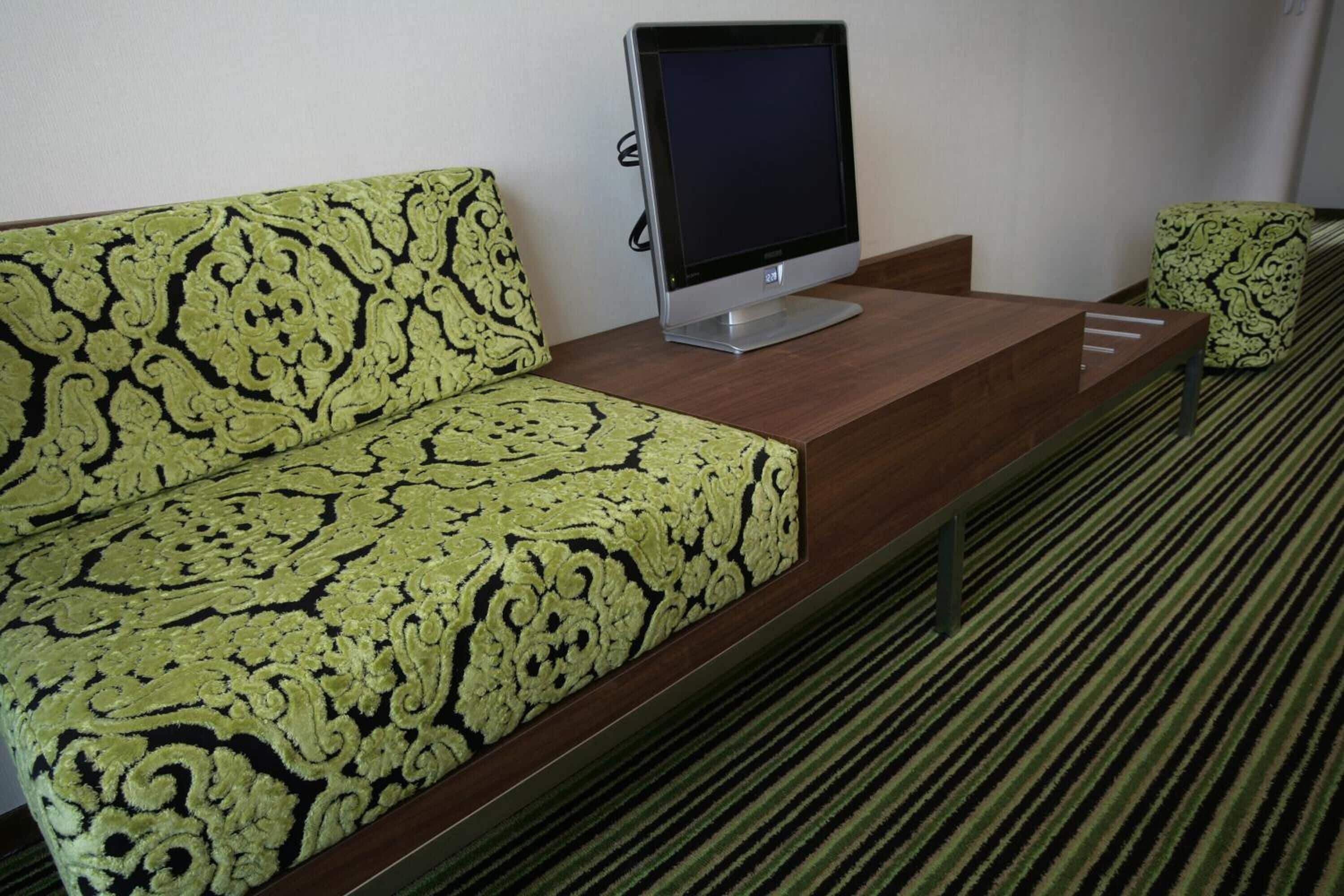 Habitación de hotel con sofá estampado, televisor de pantalla plana sobre una consola de madera y alfombra a rayas.
