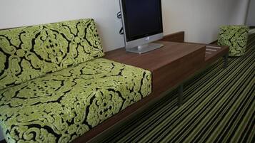 Habitación de hotel con sofá estampado, televisor de pantalla plana sobre una consola de madera y alfombra a rayas.