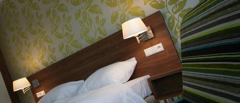 Una habitación de hotel con una cama, dos lámparas de noche y una pared decorada con un diseño de hojas.
