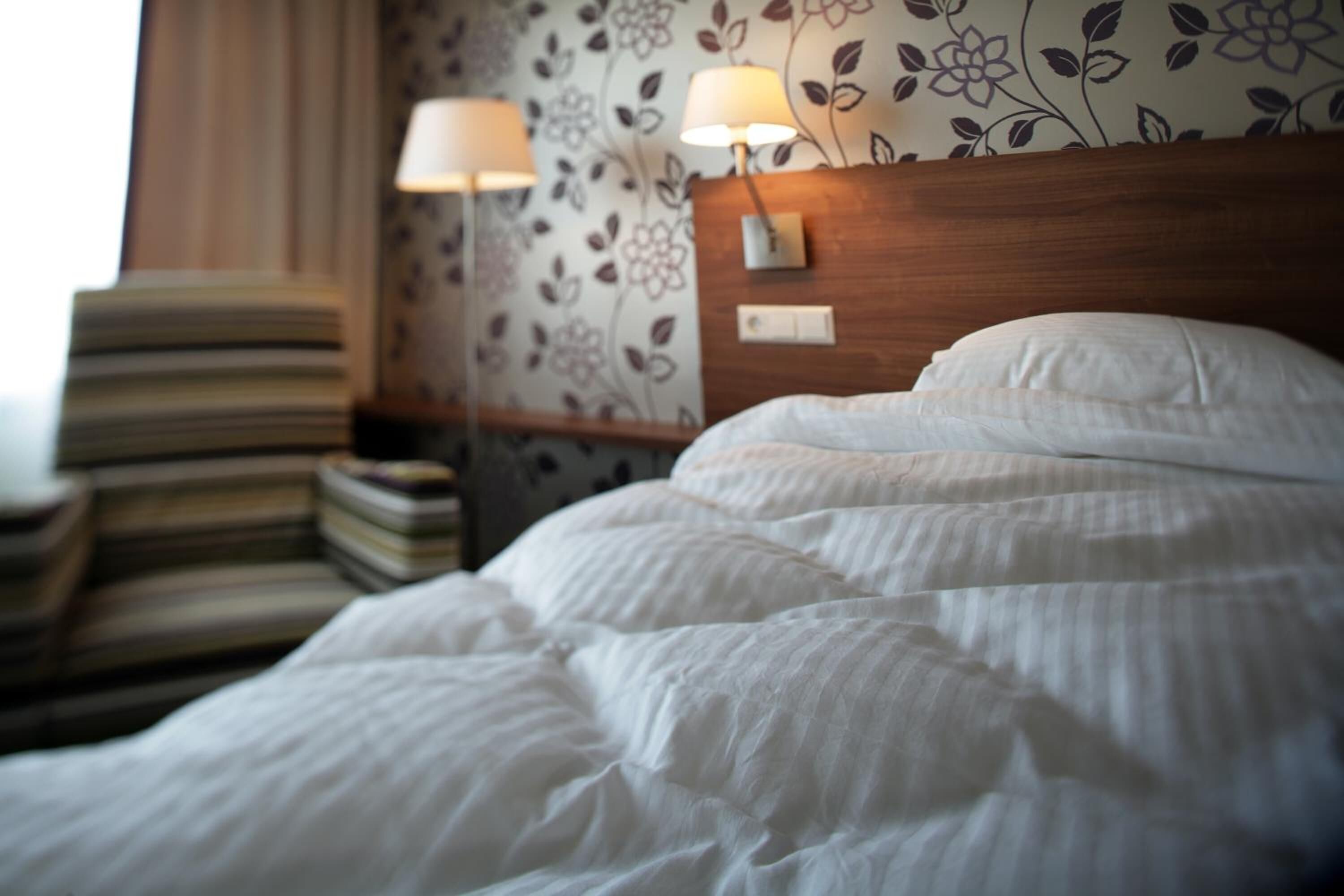 A hotel room with a neatly made bed, a striped armchair, and a nightstand with a lamp.