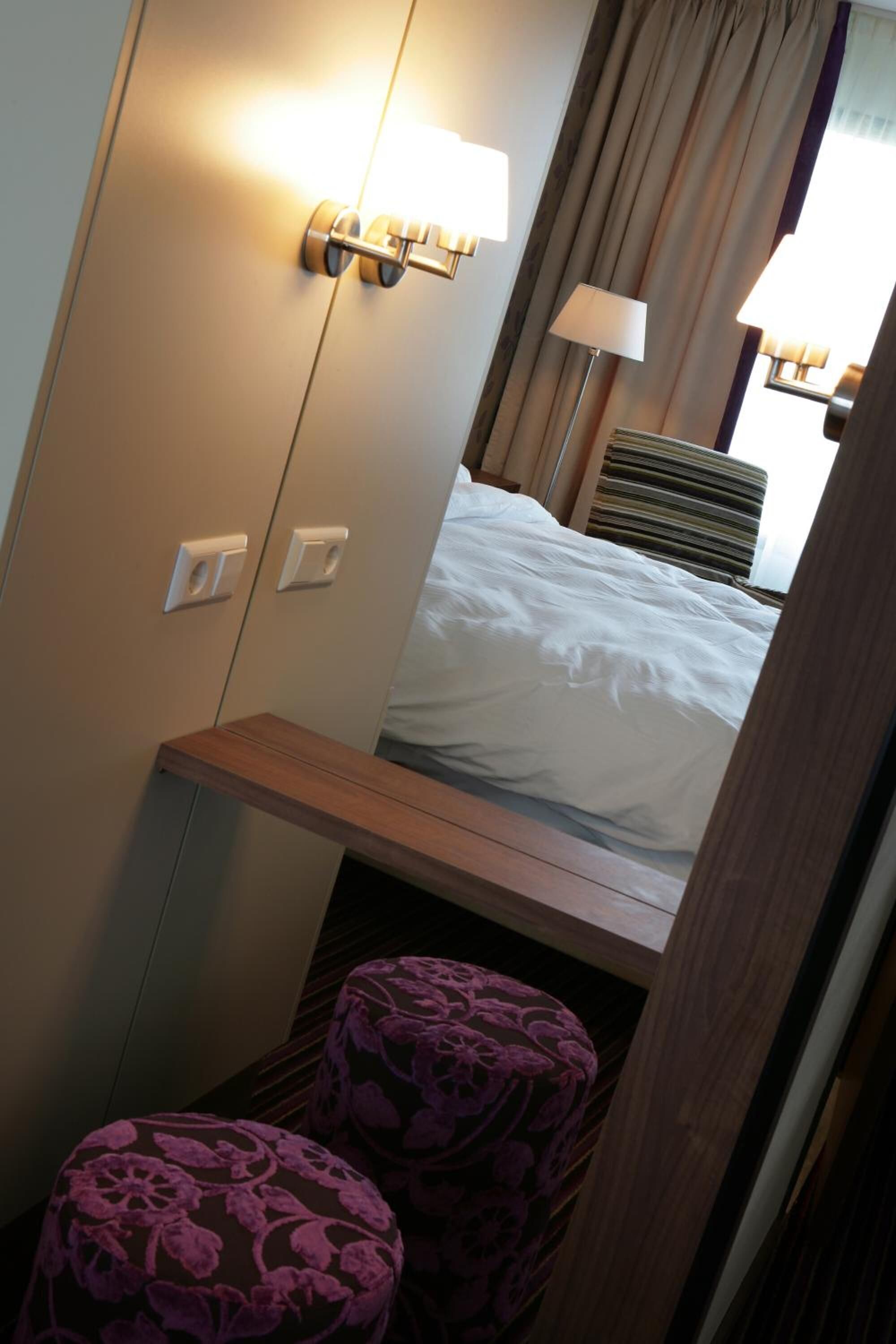 A hotel room with a bed, a bedside table, a wardrobe, and a mirror.