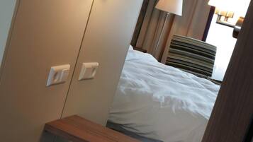 A hotel room with a bed, a bedside table, a wardrobe, and a mirror.