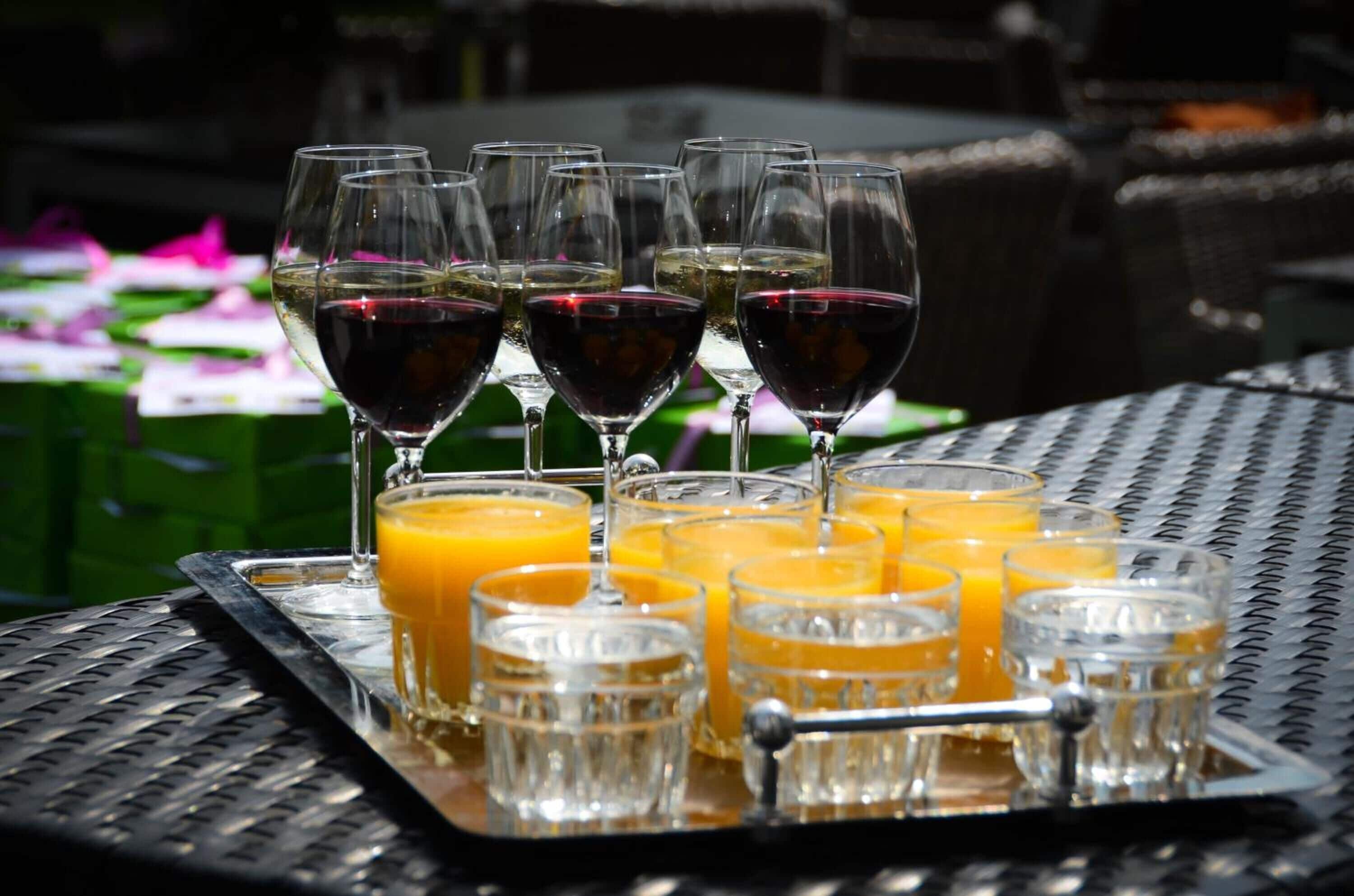 A tray with multiple wine glasses and shot glasses filled with beverages, placed on a table outdoors.