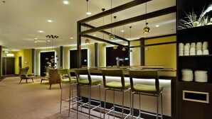Un espace bar avec des tabourets hauts, un comptoir et une étagère où sont rangées des assiettes.