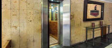 An elevator entrance with a welcome mat, a framed hotel logo, and a reception desk.