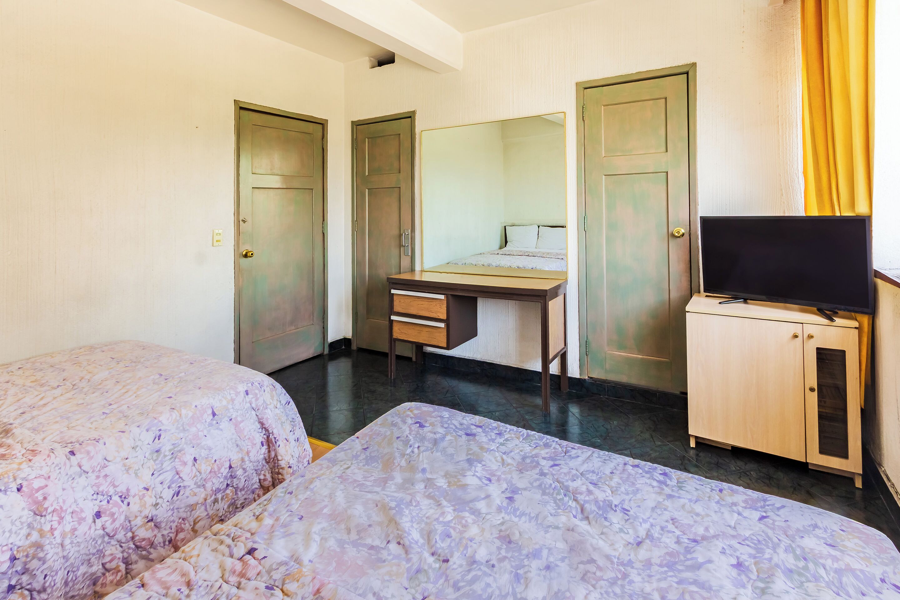 Una habitación de hotel con dos camas, un escritorio, un televisor y un armario.