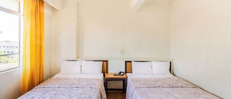 A hotel room with two beds, a ceiling fan, a nightstand with a phone, and a window with curtains.